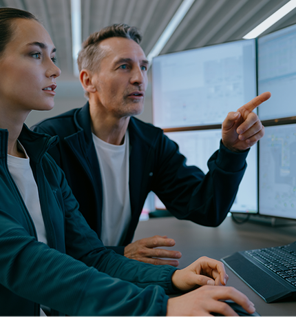 Un uomo e una donna lavorano al computer. L'uomo indica dei dati sullo schermo.