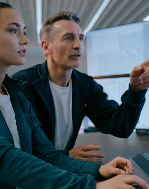 Un uomo e una donna lavorano al computer. L'uomo indica dei dati sullo schermo.